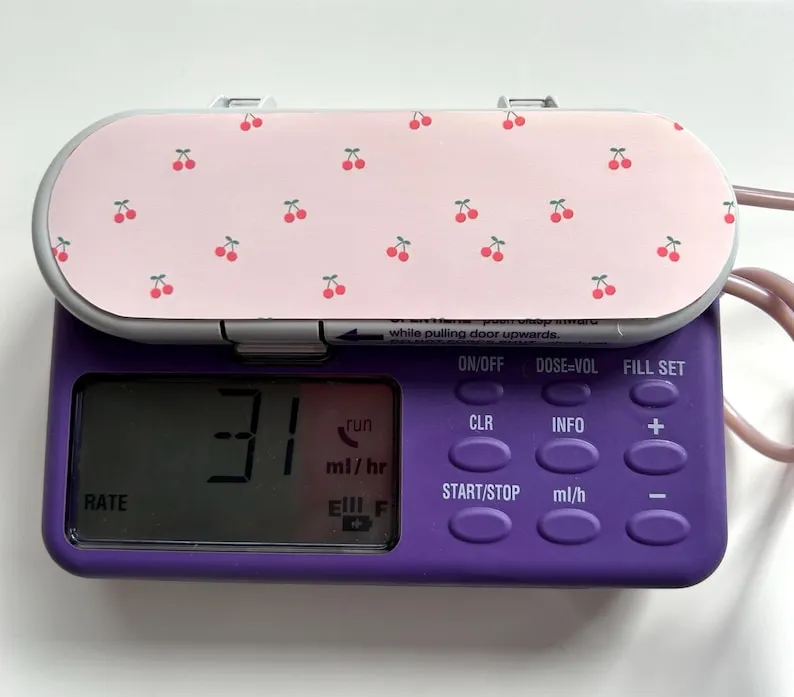 A purple Infinity feeding pump with a pink sticker covered in small red cherries stuck to the top.